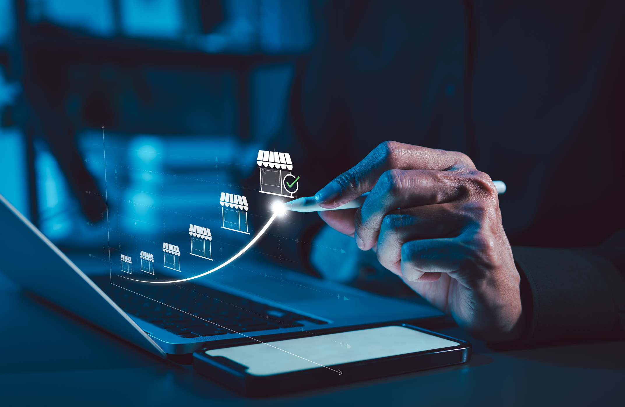 Man drawing store icons with computer, phone, and digital pen. 